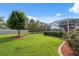 Well-manicured backyard with lush green lawn, flowering bushes, and view of the screened-in pool area at 3400 Rosebay Ct, Spring Hill, FL 34609