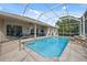 Stunning screened-in pool with a serene rock waterfall feature, surrounded by lush landscaping and patio furniture at 3400 Rosebay Ct, Spring Hill, FL 34609