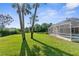 Large backyard featuring lush green grass, mature trees, and a screened-in pool area at 18244 Autumn Lake Boulevard, Hudson, FL 34667