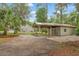 Features a large garage and covered parking with a gravel driveway surrounded by mature trees and lush greenery at 5487 Valley View Dr, Brooksville, FL 34601