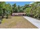 Inviting single-story home with a long driveway, red metal roof, and lush green trees in the background at 9306 21St, Tampa, FL 33612