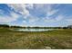 Picturesque view of a pond surrounded by green grass and trees under a bright, cloudy sky at 14008 Lugano Ct, Hudson, FL 34669