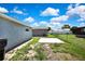 Backyard with gray house, concrete pad, and grassy area under a blue sky at 6306 Aberdeen Ave, New Port Richey, FL 34653