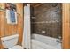 Rustic bathroom showcasing wood paneling, tile accents, tub with shower, and modern toilet at 10301 Nina Ct, New Port Richey, FL 34654
