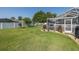 Spacious backyard featuring lush green lawn, a white fence, landscaping, and a screened-in pool at 1049 Larkin Rd, Spring Hill, FL 34608