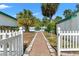 Brick path leading through a white picket fence to the lush backyard with mature palm trees at 1115 Pennsylvania Ave, Palm Harbor, FL 34683