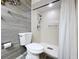 This bathroom showcases a tiled shower, a toilet, and gray wood-look walls, all well-lit at 2139 Sea Pines Ct, Spring Hill, FL 34606