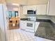Well-lit kitchen with granite countertops, white appliances, and access to dining area at 3627 Muirfield Ct # 3627, New Port Richey, FL 34655