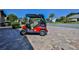 A vibrant red golf cart sits parked on a patterned stone driveway under a sunny blue sky at 8132 Summersong Ct, Spring Hill, FL 34606