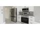 Kitchen area featuring stainless steel refrigerator, microwave, oven, gray backsplash and white cabinets at 11494 Villa Rd, Spring Hill, FL 34609