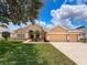 Beautiful, tan-colored single-story home with a three-car garage and a well-manicured lawn at 13248 Linzia Ln, Spring Hill, FL 34609