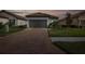 Charming single-story home at dusk, featuring a manicured lawn, paver driveway, and neutral-colored garage door at 3051 Francoa Dr, Odessa, FL 33556