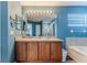 Bright bathroom featuring a double vanity, large mirror with decorative lighting, and a separate bathtub at 4094 Braemere Dr, Spring Hill, FL 34609