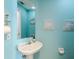 Bright bathroom featuring a pedestal sink, blue walls, decorative prints and a mirrored cabinet with a toilet at 4094 Braemere Dr, Spring Hill, FL 34609