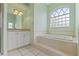 Bathroom showcasing a soaking tub beneath a window and a vanity with white cabinets and natural light at 12805 Coronado Dr, Spring Hill, FL 34609