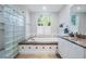 Bright bathroom featuring a tiled shower with glass blocks and a tub under a window at 2880 Chelsea N Pl, Clearwater, FL 33759