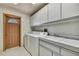 Well-lit laundry room with white washer, dryer, sink, and cabinets, and a brown door to the exterior at 5747 Fieldspring Ave, New Port Richey, FL 34655