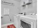 Bright laundry room with modern washer and dryer, decorative sign, storage shelf and red rug at 15241 Caravan Ave, Odessa, FL 33556