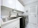Well-lit laundry room features modern washer and dryer, sink with stylish faucet, and sleek white cabinetry at 5249 Wellfield Rd, New Port Richey, FL 34655