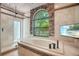A luxurious bathroom features a soaking tub and a walk-in shower, stone window, and beach on TV at 8518 Quail Hollow Blvd, Wesley Chapel, FL 33544