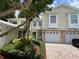 Charming yellow townhome with a brick driveway, a one-car garage, and a lush, mature landscaped front yard at 930 Woodbridge Ct, Safety Harbor, FL 34695