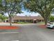 Spacious single-story clubhouse with a red awning and ample parking surrounded by mature trees and landscaping at 13001 Sawmill Way, Hudson, FL 34667