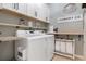 Well-organized laundry room with white cabinets, open shelves, modern washer and dryer, and decorative laundry-themed decor at 17727 Garsalaso Cir, Brooksville, FL 34604