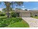 Well-maintained home exterior with brick driveway, mature tree, and a two-car garage at 2486 Deer Trail Ln, Spring Hill, FL 34606