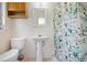 Bathroom with blue floral shower curtain, pedestal sink, toilet, and wood shelving at 507 Jewel St, Brooksville, FL 34601
