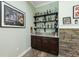 Home bar with stone accents, brown cabinets, granite counters, and floating shelving for bottles at 9431 Amidon St, Spring Hill, FL 34608