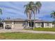 Beautiful home with a three-car garage, landscaping, and palm trees on a sunny day with blue sky at 10941 Hilltop Dr, New Port Richey, FL 34654