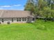 Back exterior view of a home with ample windows and a well-manicured lawn leading to a treeline at 1415 Pinewood Hills Ct, Spring Hill, FL 34606