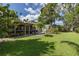 View of home's green backyard with a screened-in porch and lush landscaping at 1830 Santa Barbara Dr, Dunedin, FL 34698