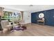 Bright living room with wood-look flooring, decor wall, and large window with lush landscaping view at 10224 Old Orchard Ln, Port Richey, FL 34668