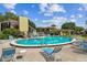 Community pool with blue lounge chairs and tables, surrounded by lush landscaping at 2101 Sunset Point Rd # 201, Clearwater, FL 33765