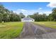 Wide driveway leading to a bright white home surrounded by lush greenery and blue skies at 2288 Rackley Rd, Brooksville, FL 34604