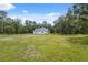Bright white home nestled in a lush green lawn, surrounded by mature trees under a blue sky at 2288 Rackley Rd, Brooksville, FL 34604