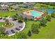 Aerial view of a community pool area, featuring a pool, sun loungers, tennis courts, and ample parking at 18558 Cortes Creek Blvd, Spring Hill, FL 34610