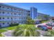 Exterior daytime shot of a multi-story light blue condo building with beautiful landscaping, a parking lot, and outdoor seating at 5555 Gulf Blvd # 315, St Pete Beach, FL 33706