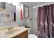 Well-lit bathroom features a shower with a purple patterned curtain, sink, and cabinets at 7701 Anaheim Ave, New Port Richey, FL 34655