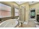 Bathroom with a soaking tub, glass-enclosed shower, neutral tile, and a large window with blinds at 11101 Ragsdale Ct, New Port Richey, FL 34654