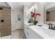 Bright bathroom featuring a double vanity, white cabinets, and a tiled shower with a dark shower head at 14645 Spellman Ct, Spring Hill, FL 34610