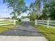 View of long asphalt drive, garages, white perimeter fence and meticulously maintained grounds at 15430 Oakcrest Cir, Brooksville, FL 34604