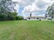 View of the home and its large grassy backyard bordered with mature trees at 2414 San Luis Rd, Holiday, FL 34691