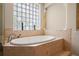 Elegant bathtub with tile surround and a glass block window providing natural light and privacy at 26221 Pheasant Run, Wesley Chapel, FL 33544