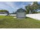 View of the shed with a roll up door and a playset beside it inside the fenced in backyard at 2027 Fentress Ct, Spring Hill, FL 34609