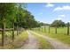 Gravel driveway leading up to the property, lined with a wooden fence and lush green trees at 34955 Blanton Rd, Dade City, FL 33523