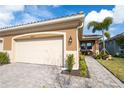 Beige house exterior with two-car garage, paved walkway, and lush landscaping at 20676 Galileo Pl, Venice, FL 34293