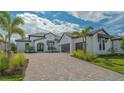 Expansive white home showcasing a paver driveway, two-car garage, tropical landscaping, and tile roof at 10629 Nicklaus Ct, Englewood, FL 34223