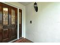 Elegant wood front door featuring decorative glass panels and an adjacent wall-mounted light fixture at 7673 Fairway Woods Dr # 706, Sarasota, FL 34238